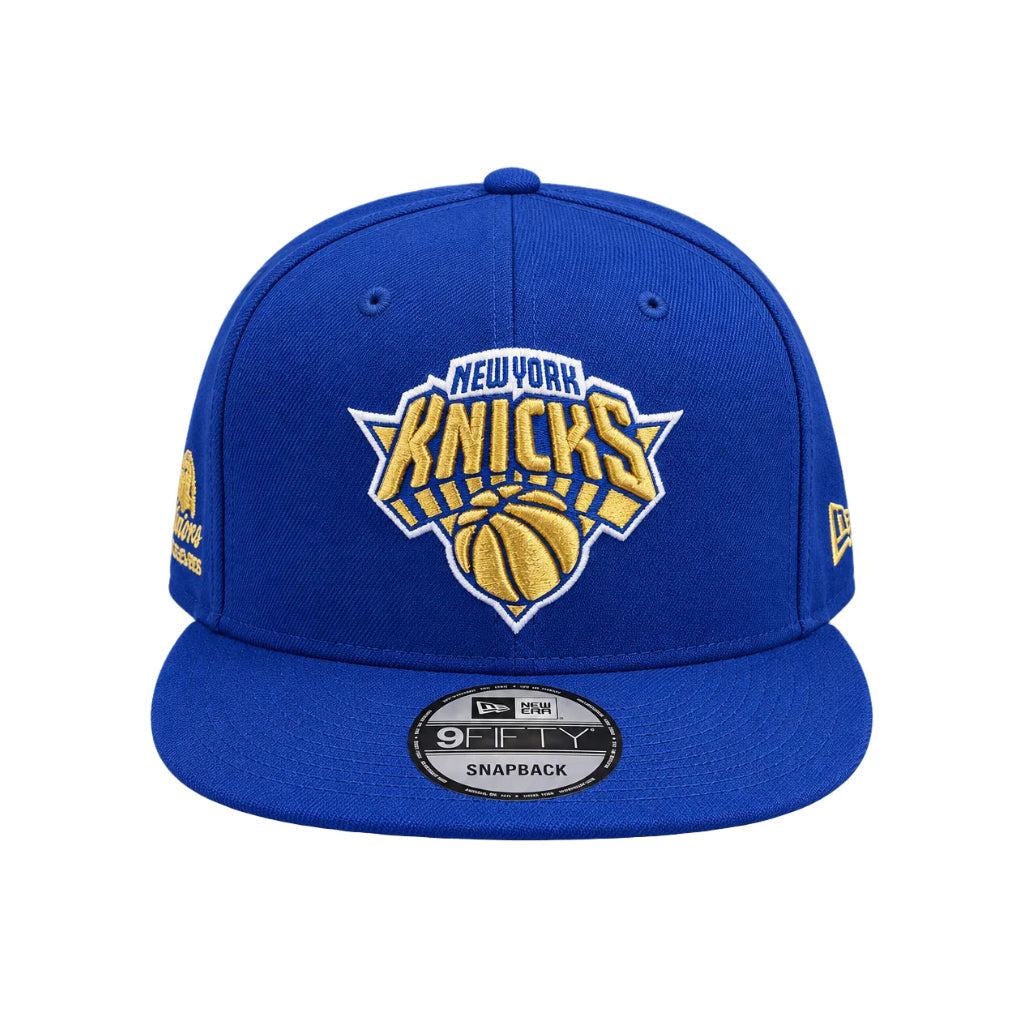 A royal blue New York Knicks snapback cap featuring a gold and white embroidered team logo on the front, with a visible New Era 9FIFTY sticker on the brim.
